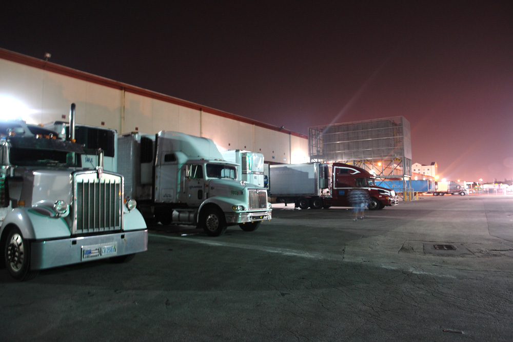 Refrigerated tractor-trailers backed into the loading dock at night